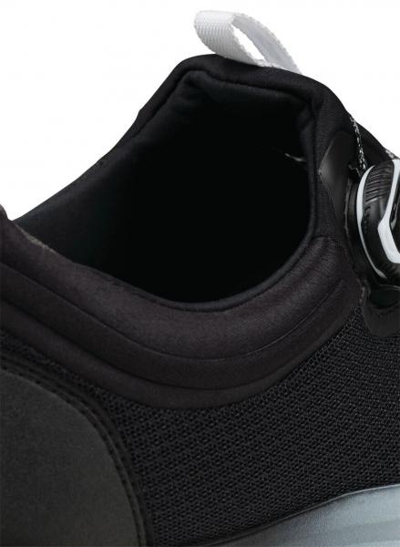 Das Bild zeigt den oberen Teil eines schwarzen Sportschuhs. Der Schuh hat ein weiches, gepolstertes Material und einen runden Ausschnitt. Oben ist ein Verschlusssystem abgebildet.