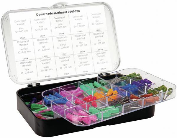 The image displays a plastic box containing various dispensing needles in different colors (green, red, orange, purple, blue) and sizes, organized into compartments. The lid is transparent.