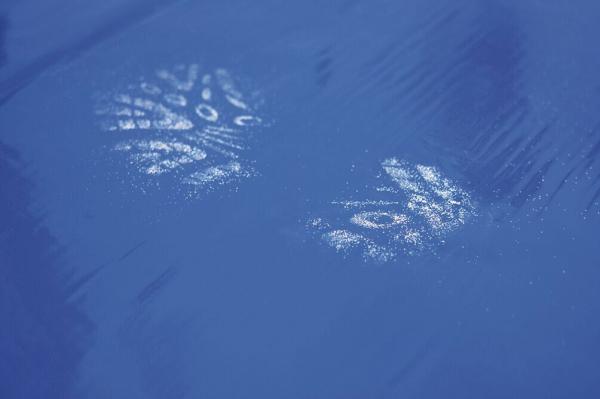 On a smooth blue surface, two footprints are visible, left with a white material. The prints show the shape of shoes.