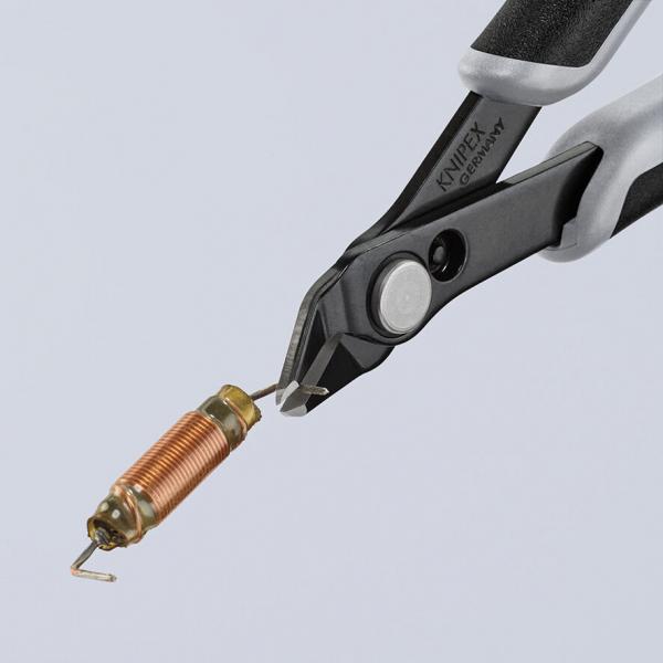 The image shows a pair of pliers with black and gray handles. It is holding a cylindrical, copper spring that has a loop at one end. The pliers have a sharp, precise shape.