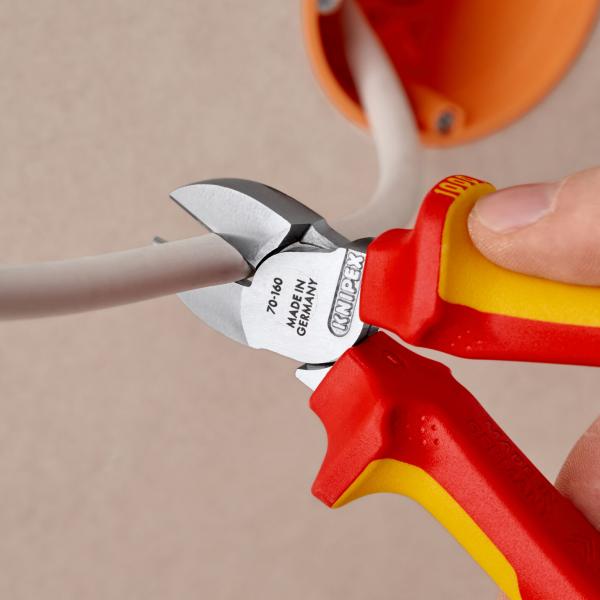 Das Bild zeigt eine Hand, die eine rote und gelbe Zange hält. Die Zange schneidet ein graues Kabel, das an einer orangefarbenen Steckdose befestigt ist.
