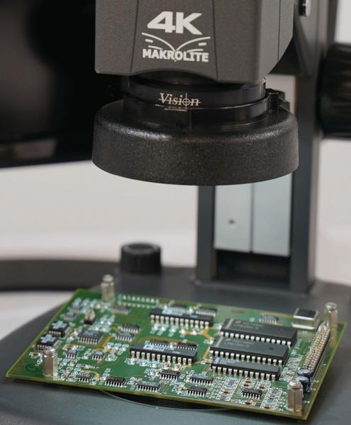 Das Bild zeigt eine grüne Leiterplatte unter einem Mikroskop mit der Aufschrift "4K Makrolite". Die Platine hat verschiedene elektronische Bauteile und ist auf einem Tisch platziert.