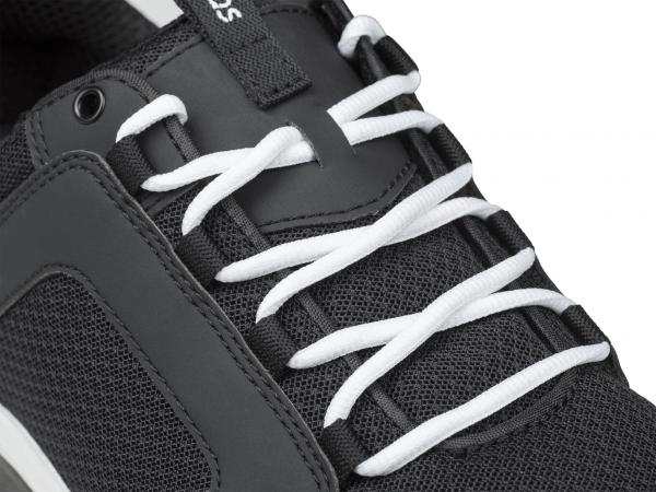 Das Bild zeigt einen schwarzen Sportschuh mit weißen, geflochtenen Schnürsenkeln. Die Oberflächenstruktur wirkt atmungsaktiv, mit einem schlichten, modernen Design.
