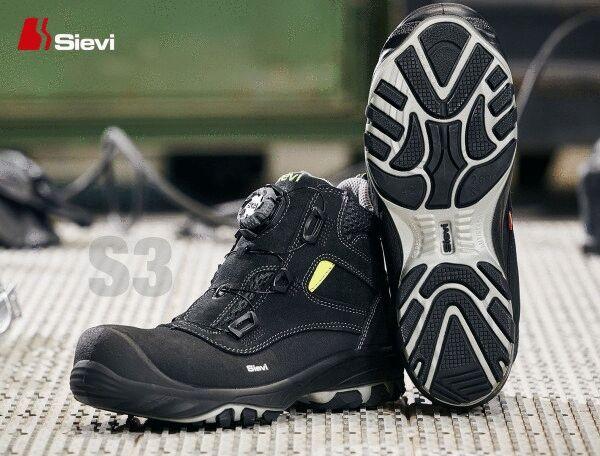 The image shows a pair of black safety boots with a modern design. The sole has a diamond-patterned profile for better grip. A yellow accent color is visible.