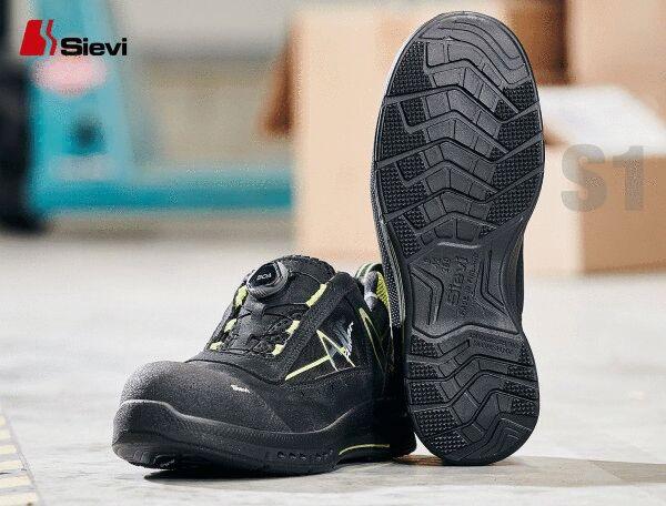 The image shows a black safety shoe with yellow accents. The sole has a textured profile for better grip. The shoe features a quick lacing system and appears sturdy.