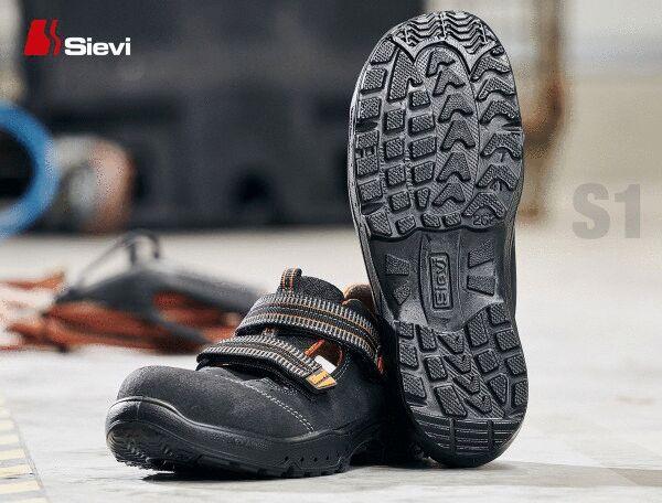 Das Bild zeigt ein Paar schwarze Sicherheitsschuhe mit einer rutschfesten Sohle. Die Schuhe haben breite Riemen über dem Fuß und sind für den Einsatz in einer industriellen Umgebung geeignet.