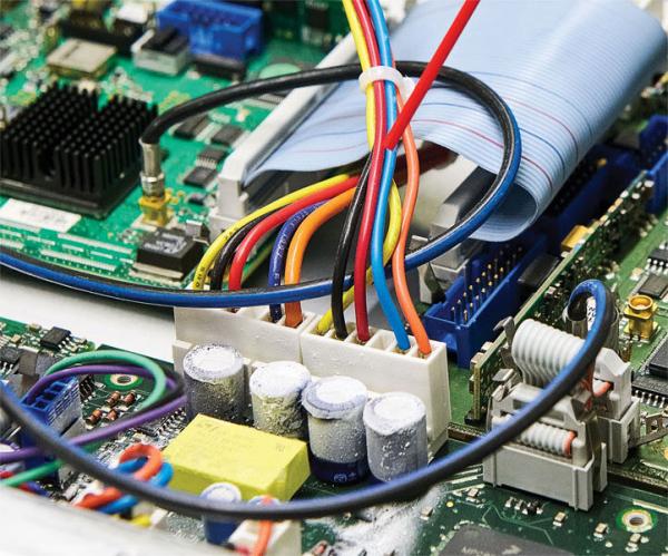 Das Bild zeigt eine elektronische Platine mit bunten Kabeln, die kreuz und quer verlaufen. Es sind verschiedene Bauteile wie Kondensatoren und Steckverbindungen sichtbar.