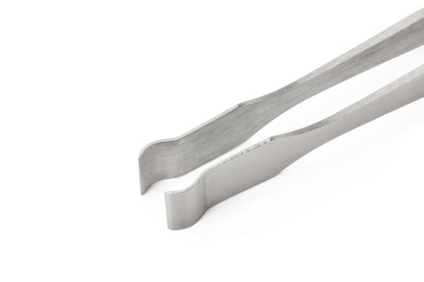 The image shows a metallic pair of tongs with two long, flat arms. The ends are bent to facilitate gripping objects. The material appears sturdy and simple.