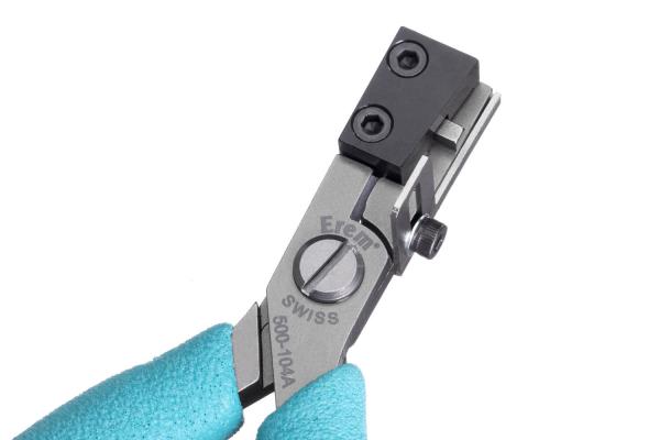 The image shows a precise pair of pliers made of silver metal with a black handle. The pliers have special notches for fine work and are held by a blue gloved hand.