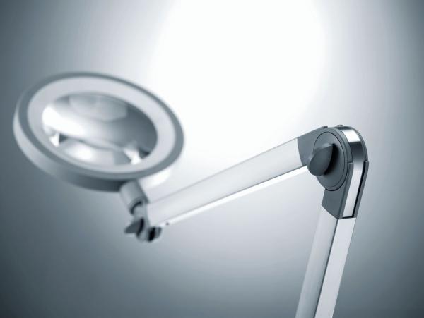 The image shows a modern light arm with a large, round lamp. The arm is swivelable and made of silver metal, with a clear, focused light inside the lamp.