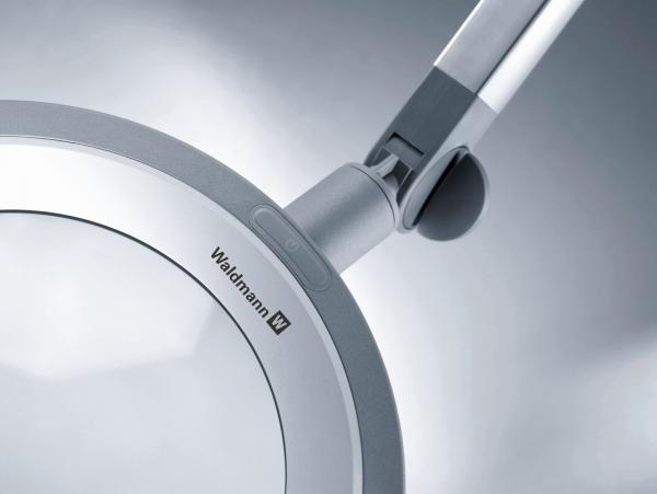 The image displays a modern magnifying glass with a large, round lens, surrounded by a slim silver frame. An adjustable arm allows for flexible positioning.