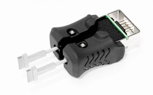 Das Bild zeigt einen schwarzen Adapter mit zwei silbernen Stiften, die nach vorne ragen. Oben ist ein Anschluss sichtbar, auf dem eine grüne und schwarze Fläche zu sehen sind.