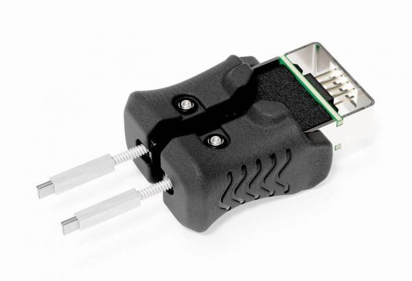 The image shows a black plug with a rectangular connection on top and two metallic pins protruding from the sides. The surface is ribbed and there are small screws.