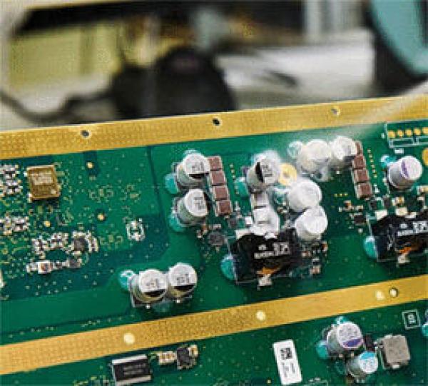 The image shows a green circuit board with many silver capacitors and black components. There are golden traces connecting the various components.