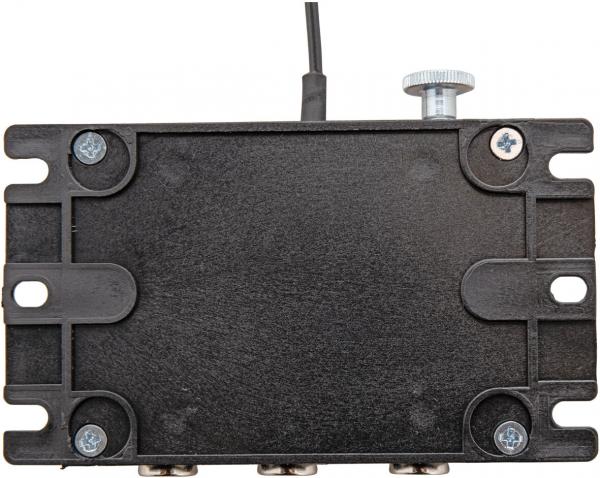The image shows a flat, rectangular, black device with a slightly textured surface. At the top, there is a cable and a rotary knob. Hexagonal screws are visible at the corners.