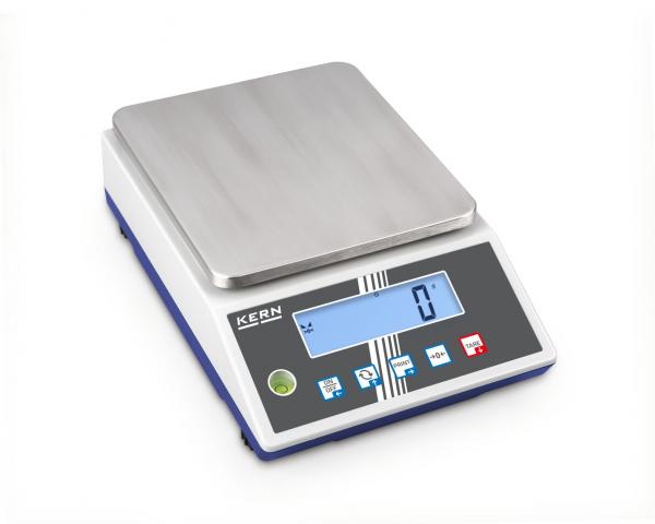 The image shows a digital scale with a smooth, rectangular metal surface. Below it, there is a display with blue digits and several buttons for operation.