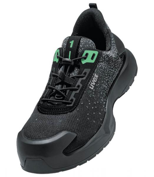Der Schuh ist ein sportlicher Sneaker mit einer schwarzen Oberfläche, die kleine, helle Punkte hat. Er hat grüne Akzente und eine stabile, gummierte Sohlenkante für guten Halt.