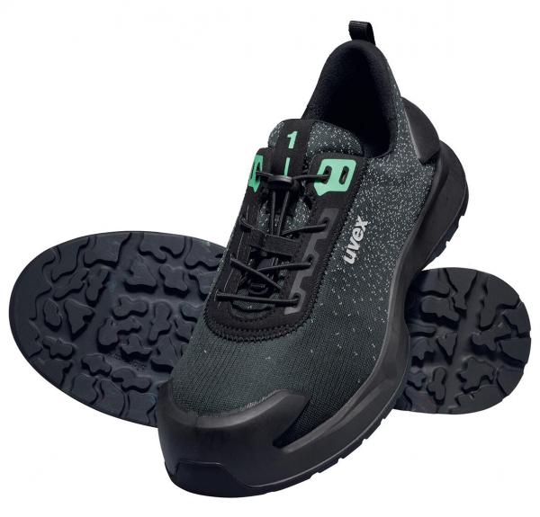 Das Bild zeigt einen schwarzen Sportschuh mit einer glatten Oberfläche und grünen Schnürsenkeln. Die Sohle hat ein strukturiertes Profil für guten Halt. Der Schuh wirkt modern und funktional.