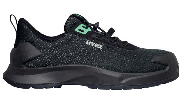 Der Schuh ist ein schwarzer, sportlicher Sneaker mit einer strukturierten Oberfläche. Er hat eine verstärkte Gummisohle und eine grüne Logoschrift an der Seite.