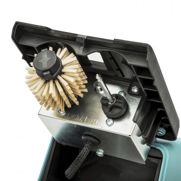 The image shows the interior of a device. A round brush with stiff bristles is mounted, next to it a metallic block with switches and a cord. The colors are primarily gray and black.