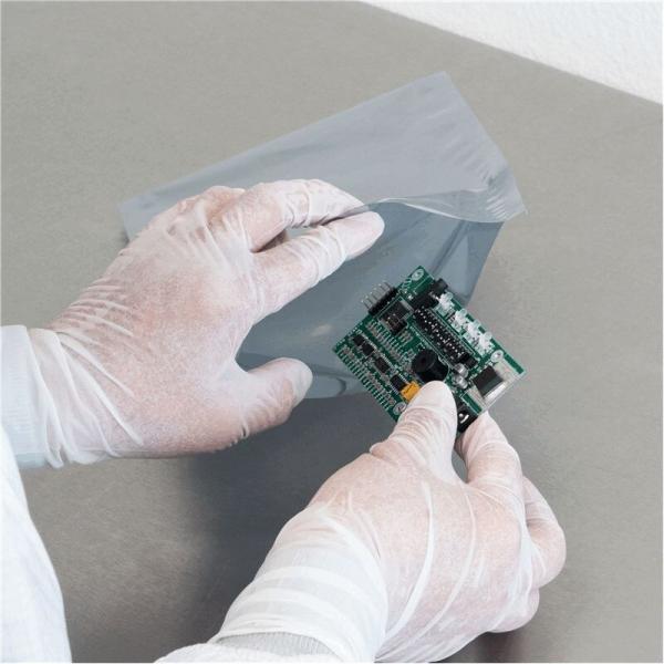 Eine Person in weißen Handschuhen hält eine grüne Platine, während sie sie aus einer grauen, stoßfesten Verpackung nimmt. Der Hintergrund ist schlicht und neutral.