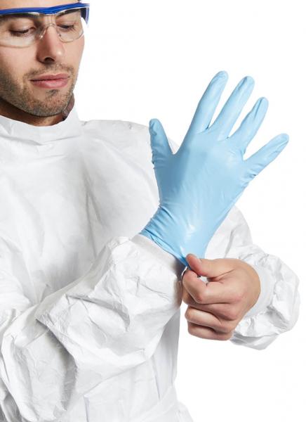Ein Mann in einem weißen Schutzanzug zieht sich einen blauen Gummi-Handschuh an. Er trägt eine Schutzbrille und konzentriert sich auf die Aufgabe.