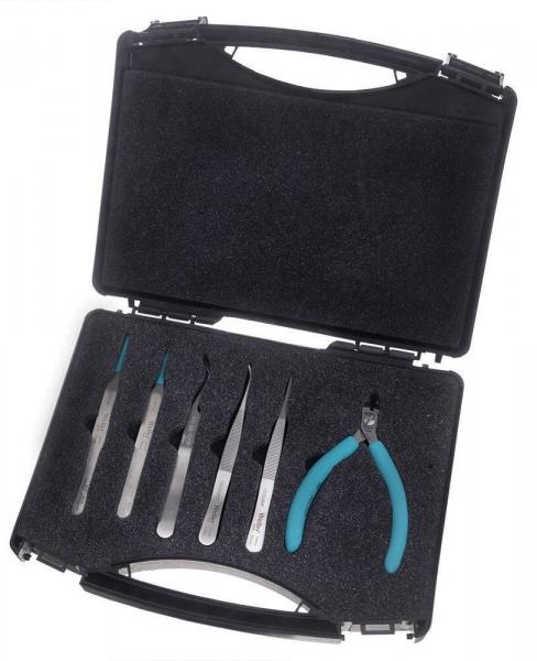 Das Bild zeigt ein schwarzes Werkzeugset mit einer Klappbox. In der Box befinden sich sechs feine Werkzeuge und eine Zange mit blauen Griffen. Die Werkzeuge sind präzise und schlank.