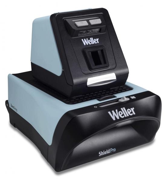 The image shows a device in black and light blue that looks like a small machine. On top, there is a vertical unit with buttons, and below, an area for inserting materials.