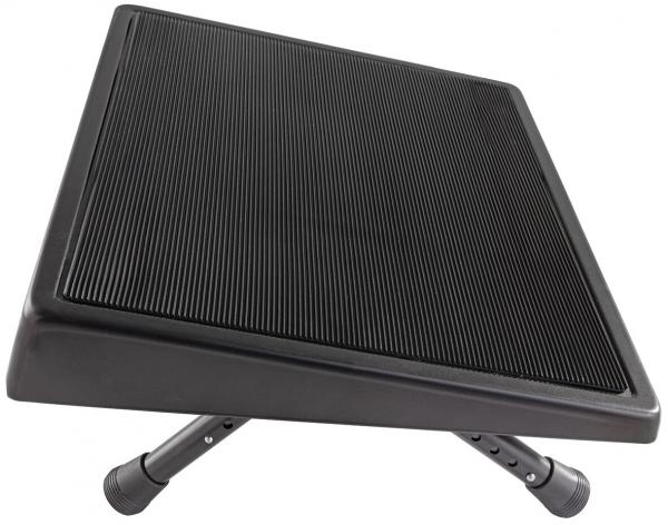 The image shows a slanted footrest with a non-slip surface. It has adjustable legs that allow for individual height adjustment. The color is black and the texture is grooved.