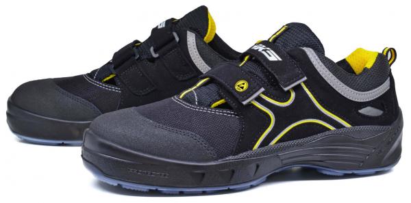 The image shows a pair of athletic shoes. They are primarily black with gray and yellow accents. The shoes feature a sturdy, non-slip sole and a convenient Velcro closure.