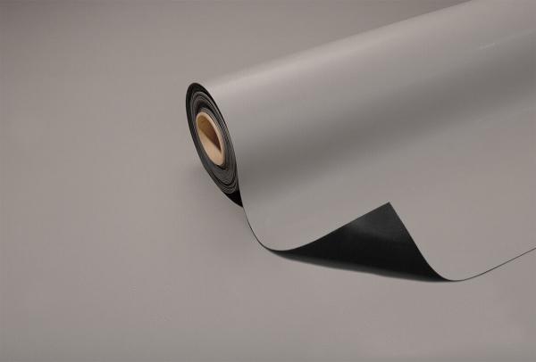 A gray carpet or mat partially lies on a surface. The roll is rolled up and displays a smooth, matte surface. The underside is dark.