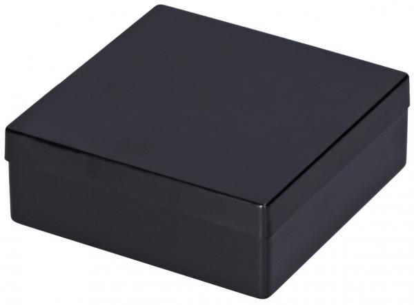 Das Bild zeigt eine quadratische, schwarze Box. Sie hat einen flachen Deckel und eine glatte Oberfläche, die glänzend wirkt. Die Kanten sind rechtwinklig und die Box steht stabil.