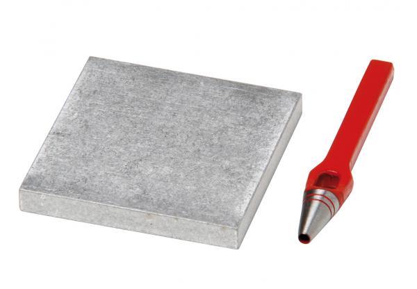 In the picture, there is a gray, square piece of metal and a red pencil with a pointed tip. The contrast between the smooth metal and the colored pencil is striking.