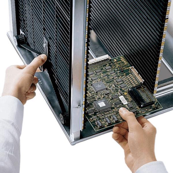 Eine Person hält eine Computerplatine in der Hand und steckt sie gerade in ein metallisches Gehäuse. Im Hintergrund sind Kühlerstreben sichtbar. Der Fokus liegt auf der Platine.