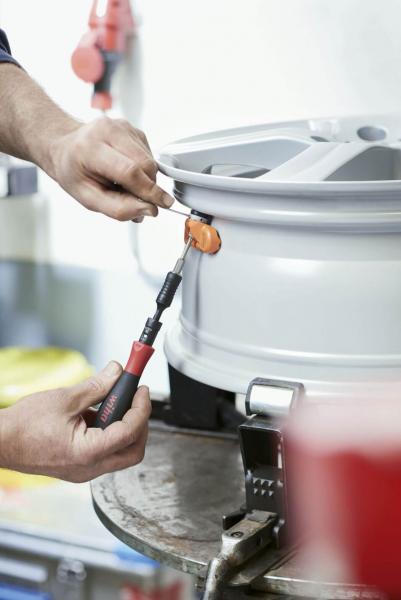 A manual workshop process: A person uses a tool to work on a silver rim. In the background, workshop utensils and a bright environment can be seen.