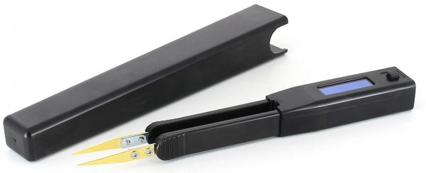 The image displays a black device with two golden clamps, which is open, and a rectangular casing. Next to the device, there is a black cap or protective cover.