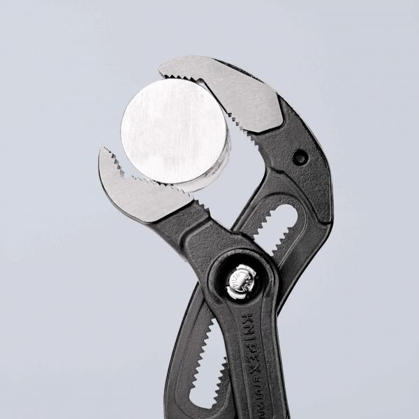 The image shows a pair of pliers with a gray, grippy plastic handle. It is holding a round, silver plate. The pliers have a straight cutting edge and a serrated area for better grip.