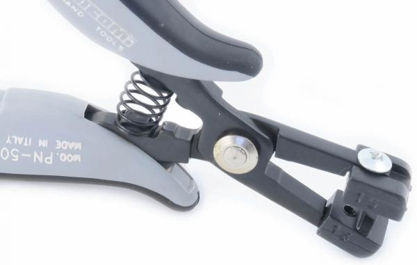 The image shows a tool with two contoured, ergonomic handles. At the end, there is a mechanism with a spring and an opening that is used for gripping or cutting.