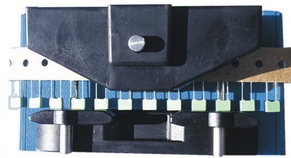The image shows a device with a black top part and a blue base. Below, two round rollers are visible. On the side, there are several green and white switches or buttons.
