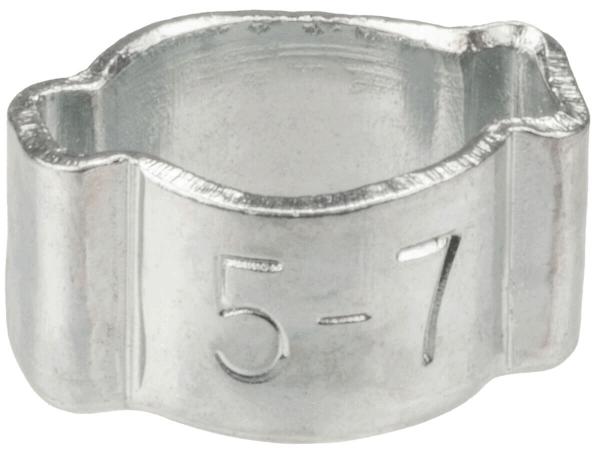 The image shows a small, silver metal bracket. It has a round opening in the center and is slightly wavy at the top and bottom. On the side, the numbers "5-7" are engraved.