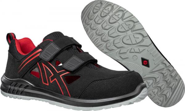 The image shows a pair of black shoes with red accents. They have a sporty shape and Velcro fasteners. The sole is grippy and features a textured pattern.
