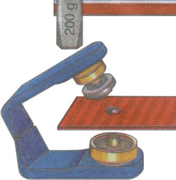The image shows a lever device with a grey weight of 200 g. A screw with a roller presses on a red metal piece to secure it.