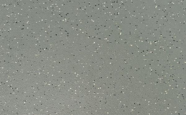 Die Oberfläche ist in einem matten Grauton gehalten, mit vielen kleinen, glänzenden Partikeln in Schwarz und Weiß, die unregelmäßig verteilt sind. Es wirkt strukturiert und modern.