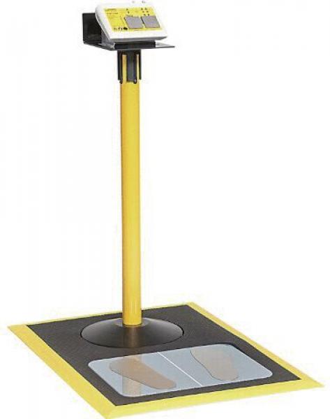 The image shows a yellow, upright column with a display on top. Below it is a square platform with round and oval imprints. The entire area is in yellow and black.