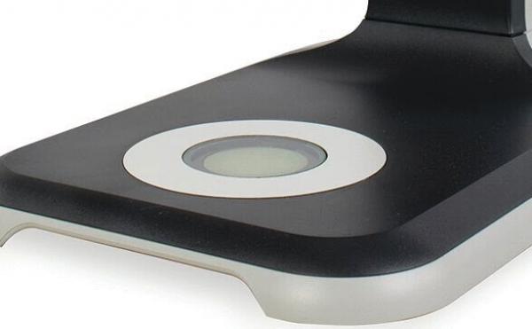 The image shows a modern, black charging station with a circular, white area in the center. The edges are rounded, and the surface appears smooth and shiny.