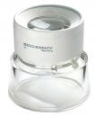 Preview: The image shows a magnifying glass in a compact, round design. At the top is a clear lens insert, below which is a slightly curved base made of transparent plastic. The surface is predominantly white.