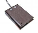 Preview: The image shows a rectangular, flat device with a rough surface texture. It has two push buttons on top and a cable that leads out from the side. The color is dark brown.