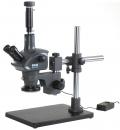 Preview: The image shows a microscope with a stable base. It has two eyepieces, an elongated objective, and a rotatable stage. A cable runs from the base. It is in dark gray.