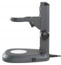 Preview: The image shows a gray magnifying device on a stable base. It has a short arm with a lens and controls for adjustment. A switch is located on the bottom.