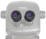 Preview: The image shows a binocular microscope with two large, round eyepieces. The surface is light gray with the 
